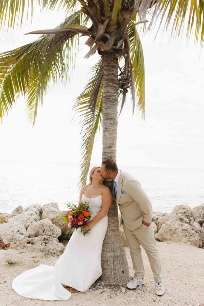 A bride and groom kissing in front of a palm tree at their elopement in Key West, Florida