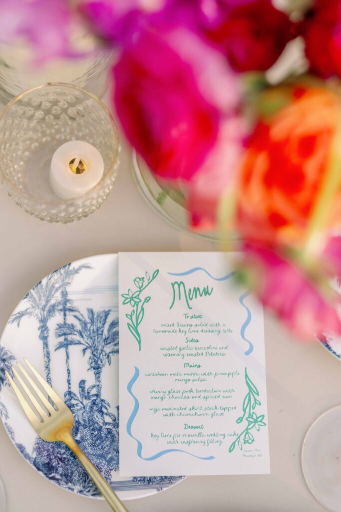 A vibrant garden wedding reception in Key West at The Ernest Hemingway Home. This photo features a photo of the handwritten menu, plate, and floral arrangement.